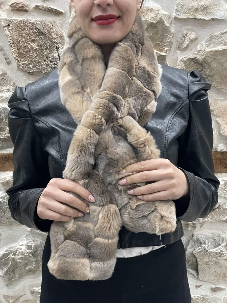 May include: A brown faux fur scarf with a textured pattern. The scarf is worn around the neck of a person wearing a black leather jacket.