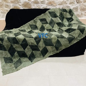 Puede incluir: Una manta de tiro con estampado geom&eacute;trico verde y negro con las letras "VFC" en azul sobre la tela. La manta est&aacute; drapeada sobre un sof&aacute; negro.