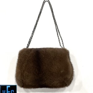 May include: A brown fur clutch bag with a silver chain strap.