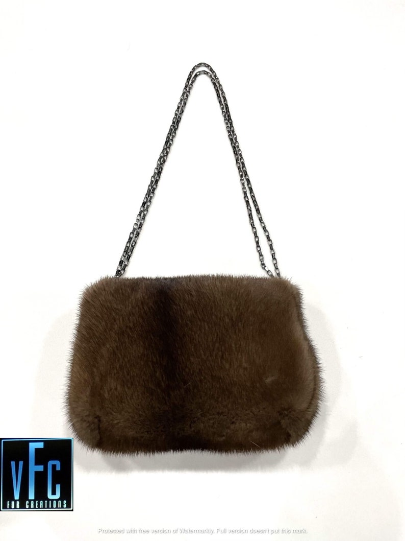 May include: A brown fur clutch bag with a silver chain strap.