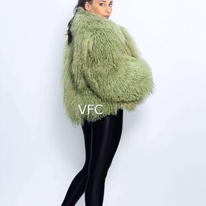 May include: A woman in a light green faux fur jacket and black leggings. The jacket has a shaggy texture. The leggings are shiny. She is also wearing clear heeled sandals. The letters "VFC" are visible on the jacket.