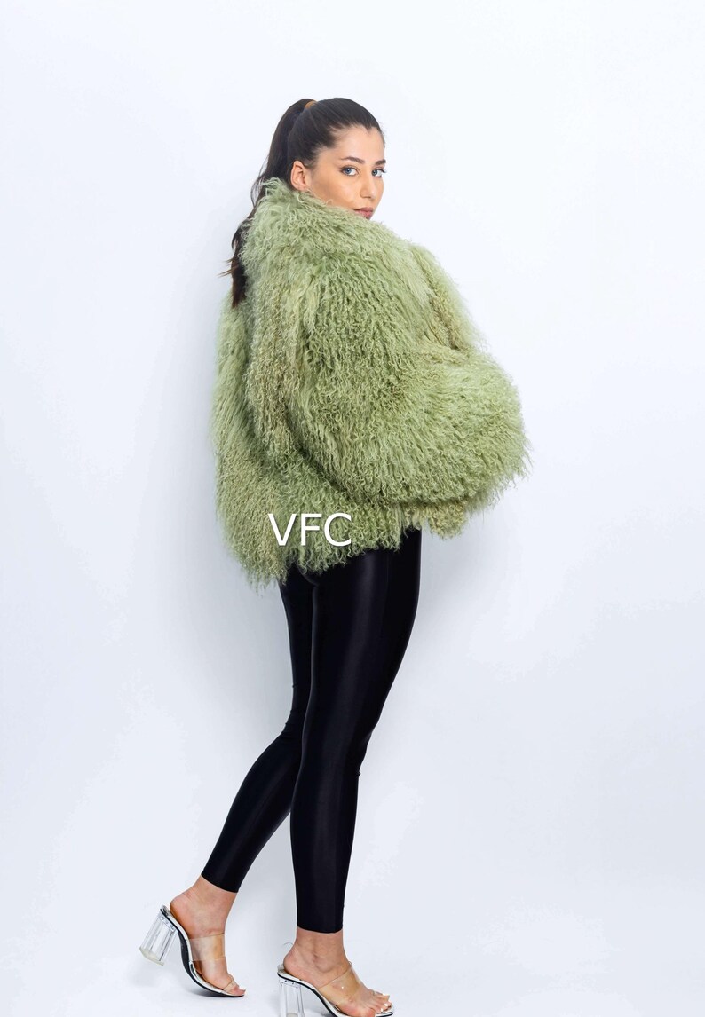 May include: A woman in a light green faux fur jacket and black leggings. The jacket has a shaggy texture. The leggings are shiny. She is also wearing clear heeled sandals. The letters "VFC" are visible on the jacket.