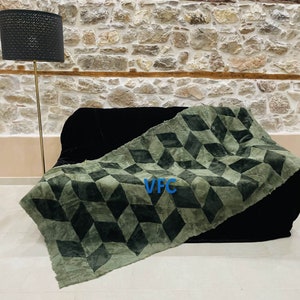 Puede incluir: Una manta de tiro verde y negra con estampado geom&eacute;trico con el texto "VFC" en el centro.