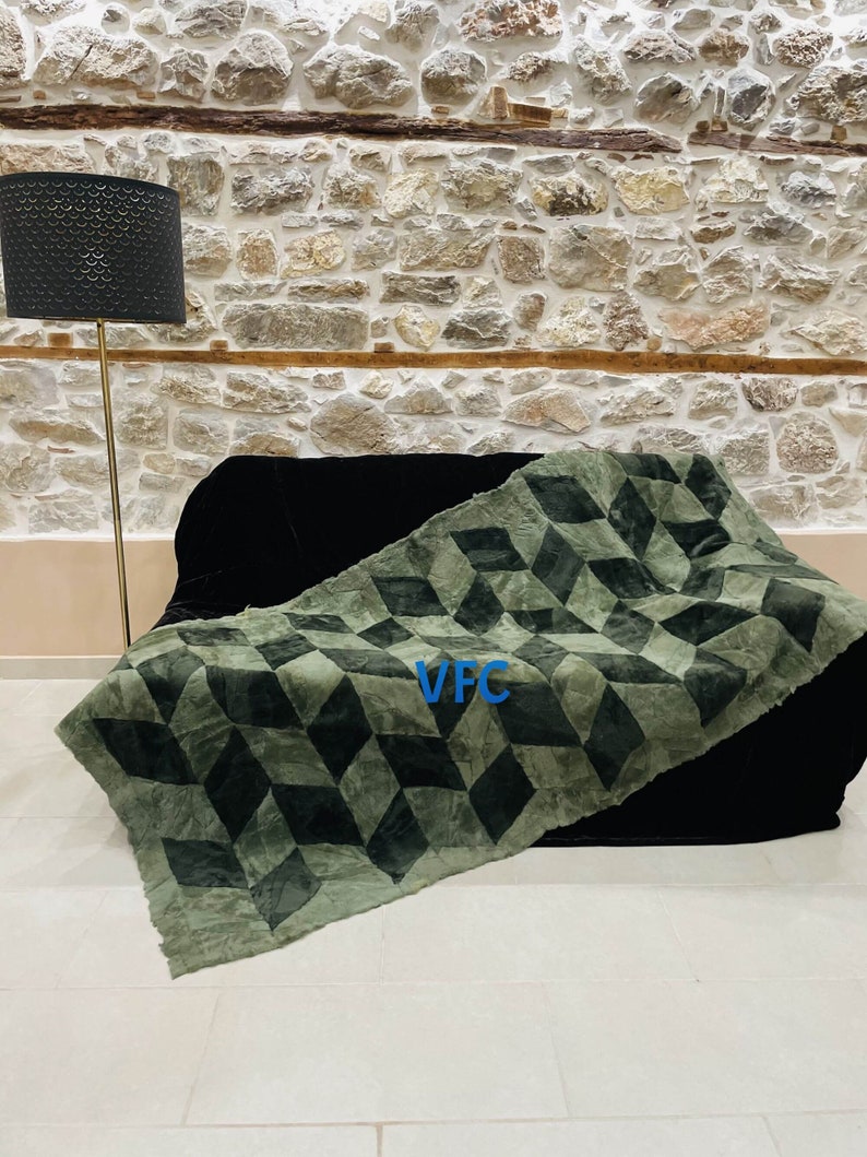 Puede incluir: Una manta de tiro verde y negra con estampado geom&eacute;trico con el texto "VFC" en el centro.