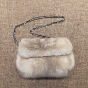 May include: A small, light brown fur clutch bag with a silver chain strap.