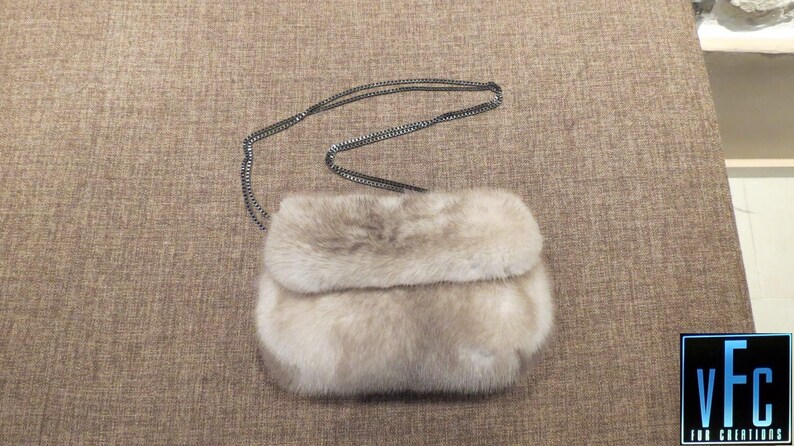 May include: A small, light brown fur clutch bag with a silver chain strap.
