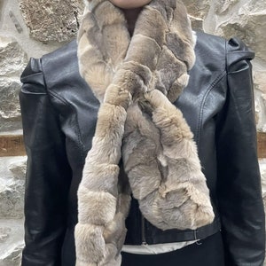 May include: A light brown faux fur scarf with a woven pattern. The scarf is worn around the neck of a person wearing a black leather jacket.