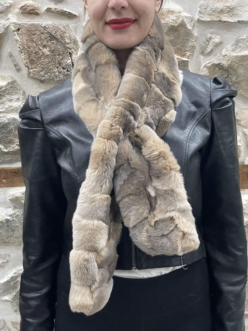 May include: A light brown faux fur scarf with a woven pattern. The scarf is worn around the neck of a person wearing a black leather jacket.
