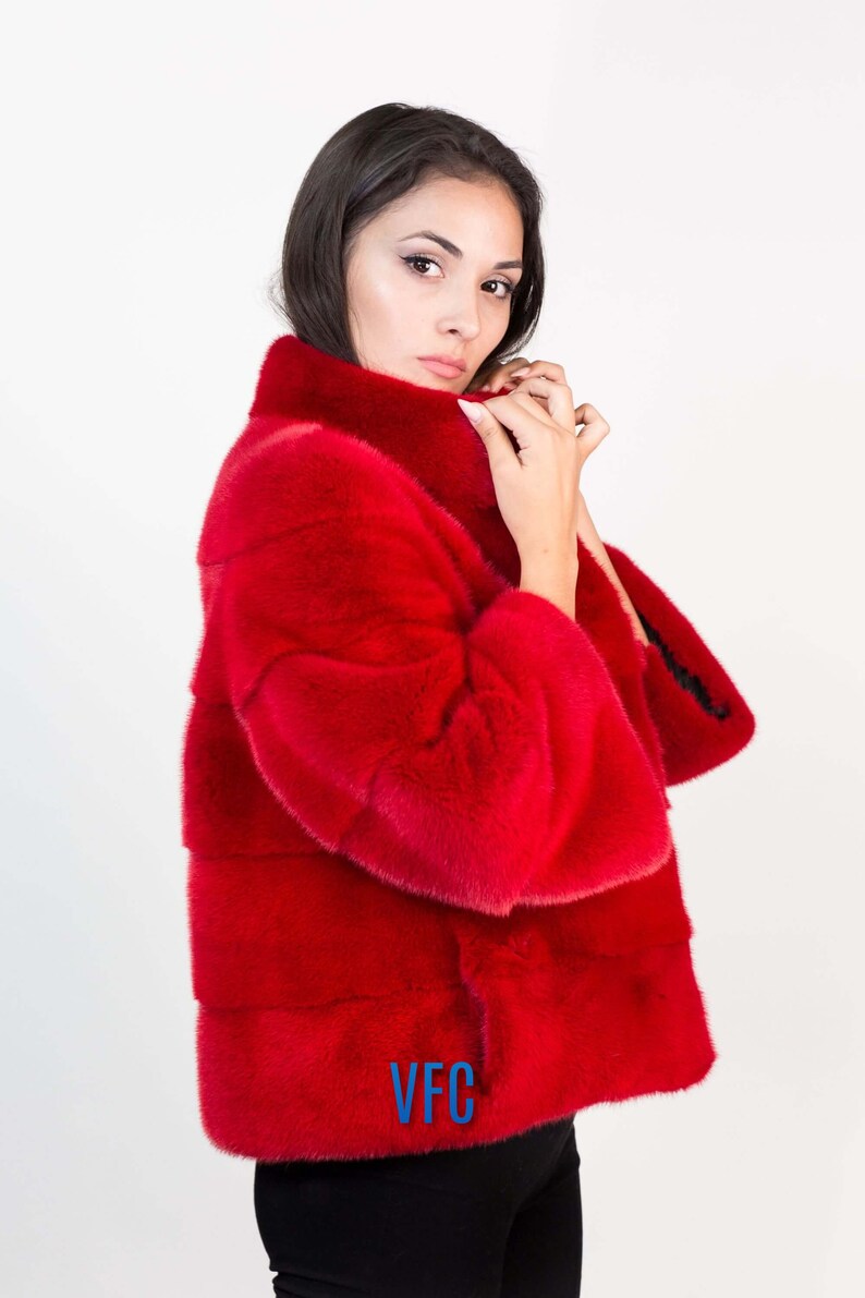 Peut inclure: Un manteau en fourrure rouge avec un col montant. Le manteau porte le logo VFC sur le devant.
