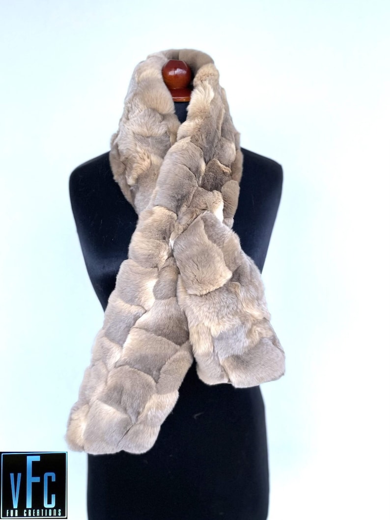 May include: A light brown fur scarf with a quilted pattern. The scarf is displayed on a black mannequin.