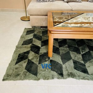 Puede incluir: Una alfombra de color verde y negro con un patr&oacute;n geom&eacute;trico y una mesa de caf&eacute; de madera con tapa de vidrio. La alfombra tiene una textura peluda.