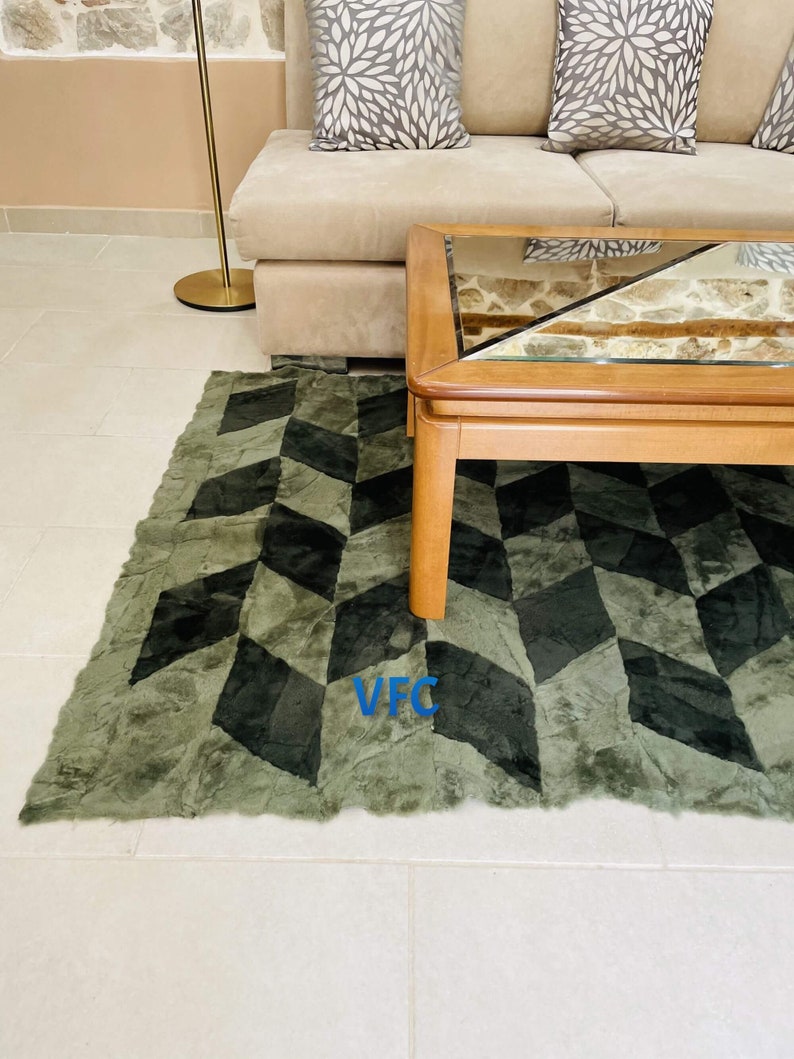 Puede incluir: Una alfombra de color verde y negro con un patr&oacute;n geom&eacute;trico y una mesa de caf&eacute; de madera con tapa de vidrio. La alfombra tiene una textura peluda.