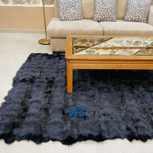 May include: A black fur rug with a light brown border. The rug is in a living room setting with a couch and a coffee table. The rug has the letters "VFC" in blue on it.