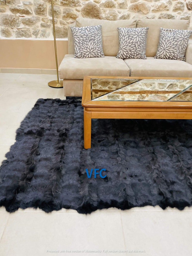 May include: A black fur rug with a light brown border. The rug is in a living room setting with a couch and a coffee table. The rug has the letters "VFC" in blue on it.
