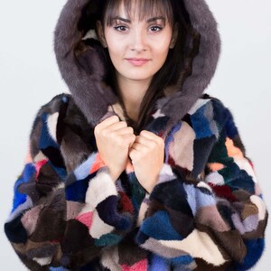 Puede incluir: Una chaqueta de piel de patchwork colorida con una capucha grande. La chaqueta est&aacute; hecha de pieles de diferentes colores, incluyendo marr&oacute;n, negro, azul, rosa y blanco. La capucha est&aacute; forrada con una piel marr&oacute;n oscura.