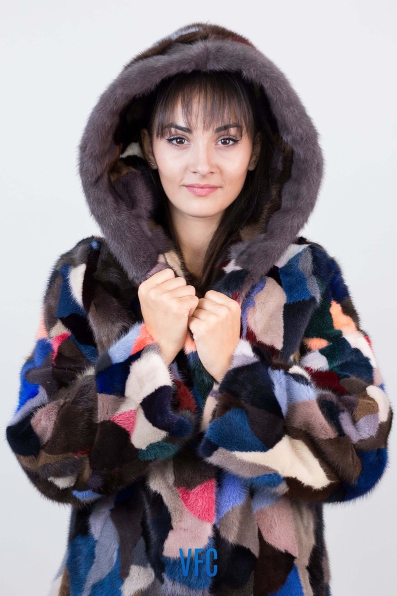 Puede incluir: Una chaqueta de piel de patchwork colorida con una capucha grande. La chaqueta est&aacute; hecha de pieles de diferentes colores, incluyendo marr&oacute;n, negro, azul, rosa y blanco. La capucha est&aacute; forrada con una piel marr&oacute;n oscura.