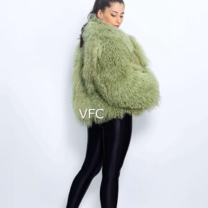May include: A light green faux fur jacket with a textured finish. The jacket is worn with black leggings and clear heeled sandals. The letters "VFC" are visible on the jacket. The model is facing away from the camera.