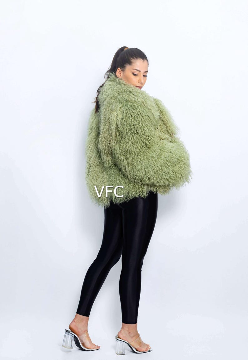 May include: A light green faux fur jacket with a textured finish. The jacket is worn with black leggings and clear heeled sandals. The letters "VFC" are visible on the jacket. The model is facing away from the camera.