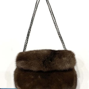 May include: A brown fur clutch bag with a silver chain strap.