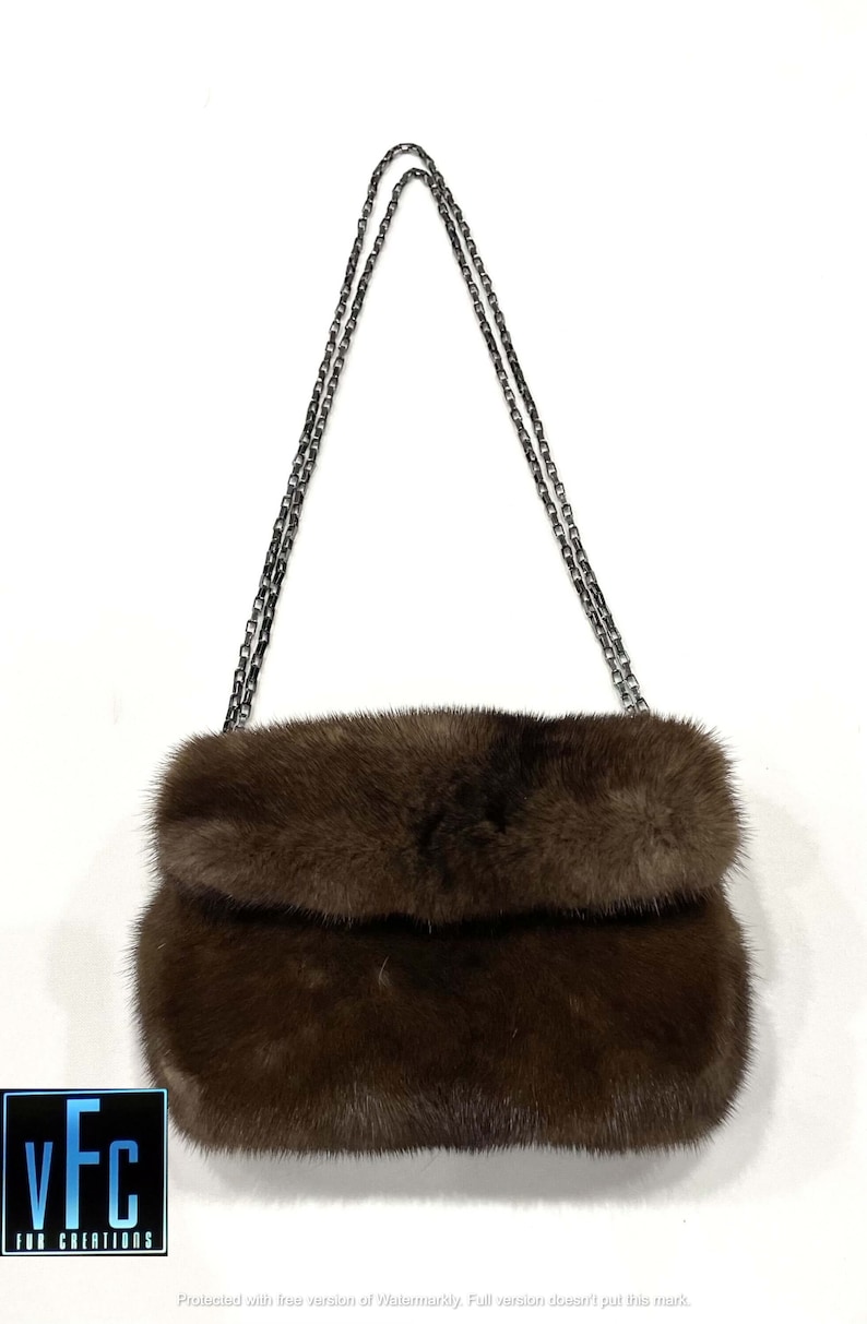 May include: A brown fur clutch bag with a silver chain strap.