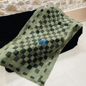 Pode incluir: Uma manta de pele de carneiro xadrez verde e preta. A manta est&aacute; dobrada e colocada em um sof&aacute; preto.