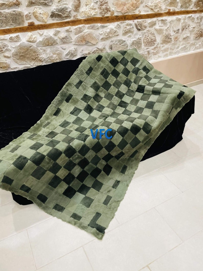Pode incluir: Uma manta de pele de carneiro xadrez verde e preta. A manta est&aacute; dobrada e colocada em um sof&aacute; preto.