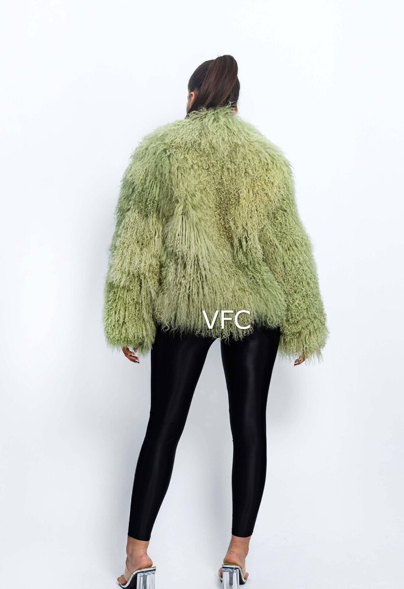 May include: A light green faux fur jacket with a textured appearance. The jacket has a round collar and long sleeves. The model is wearing black leggings and clear heeled sandals. The text "VFC" is visible on the jacket.