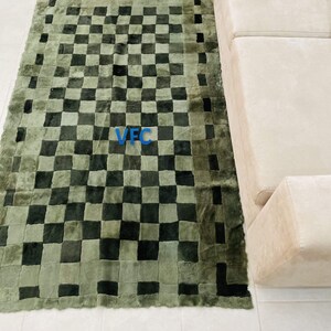 Pode incluir: Um tapete xadrez verde e preto com uma borda ligeiramente desfiada. O tapete &eacute; feito de um material macio e felpudo e tem um design &uacute;nico de patchwork.