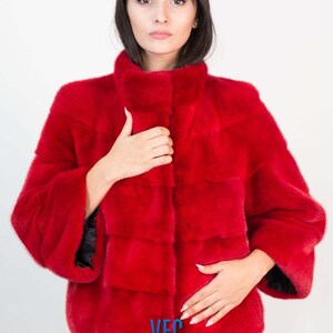 Peut inclure: Une veste en fourrure rouge avec un col montant et un logo VFC sur le devant.