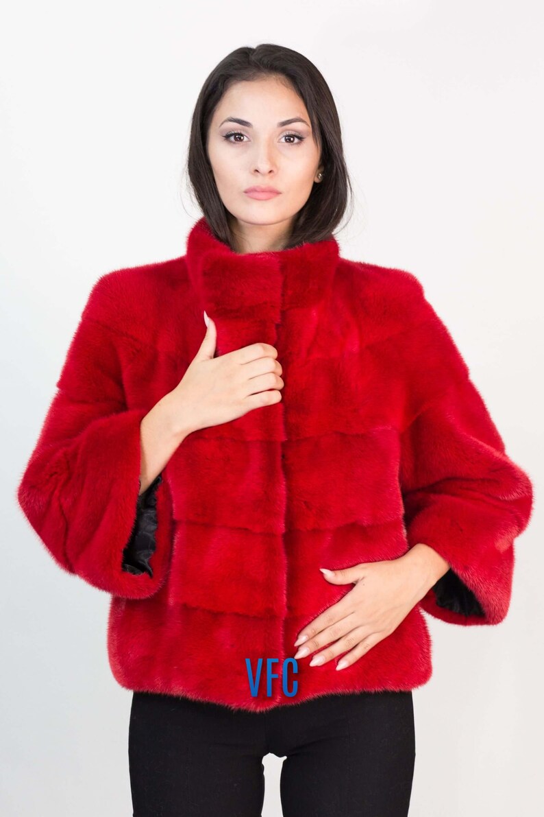 Peut inclure: Une veste en fourrure rouge avec un col montant et un logo VFC sur le devant.