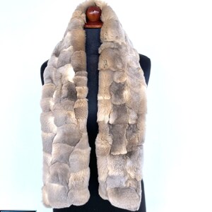 May include: A light brown faux fur scarf with a patchwork design. The scarf is displayed on a black mannequin.