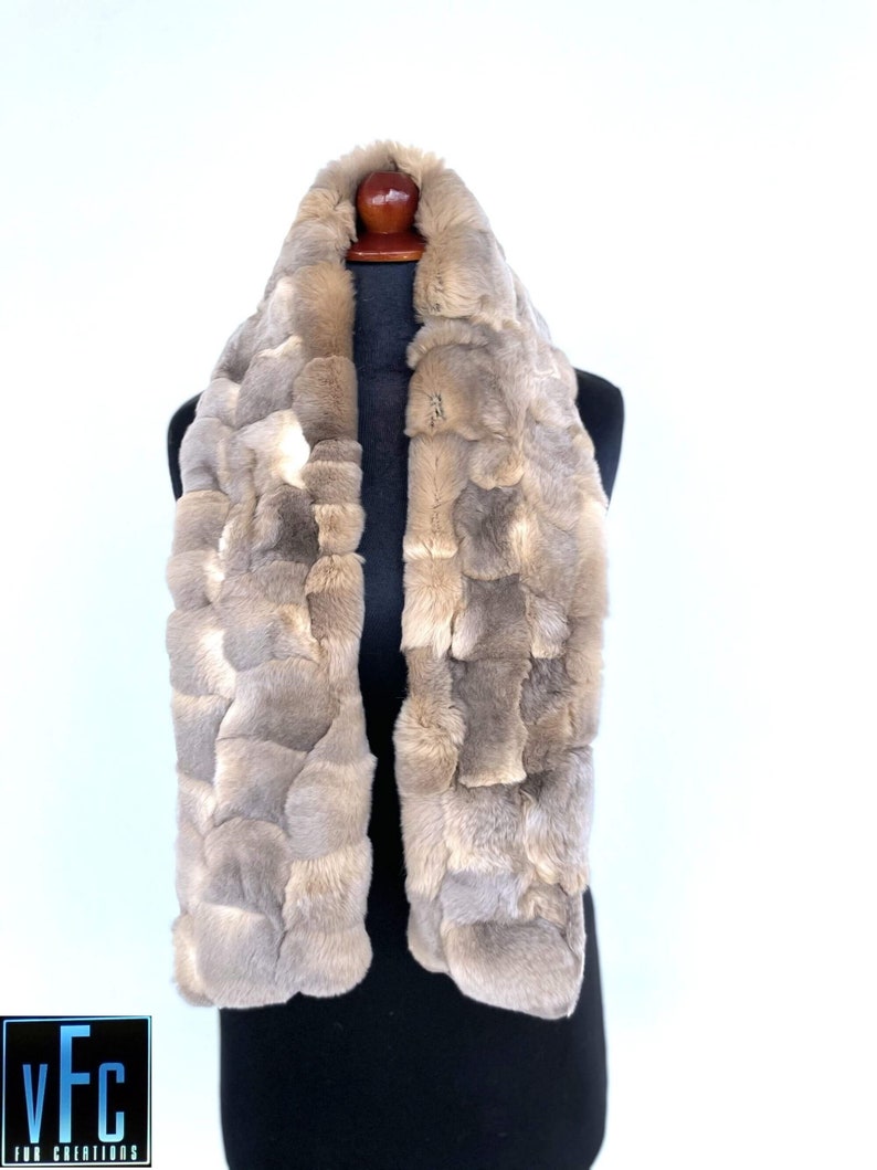 May include: A light brown faux fur scarf with a patchwork design. The scarf is displayed on a black mannequin.