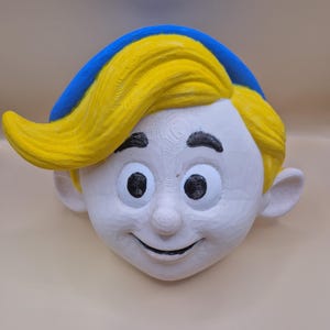 May include: A carved wooden face with a smiling expression. The face is painted white with black eyes and eyebrows. The hair is yellow and the hat is blue. The carving is likely a decorative item or a piece of art.