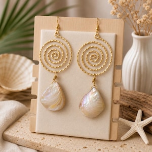 May include: A pair of gold-toned earrings featuring a textured spiral wire design at the top. Each earring hangs from a hook and includes a teardrop-shaped iridescent shell pendant suspended from the centre of the metal spiral component.