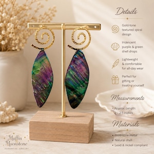 May include: Dangle earrings featuring gold-tone metal spiral tops and iridescent purple and green shell drops. The earrings are displayed on a T-shaped stand. Text on the image includes Details, Measurements, and Materials, noting a length of 5-6.4 cm.