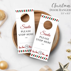 May include: Two white Christmas door hangers, each 3.5 x 8.5 inches, with a red and green striped border. The text reads "Santa PLEASE STOP HERE" in red and black. A reindeer and sleigh graphic is at the bottom.