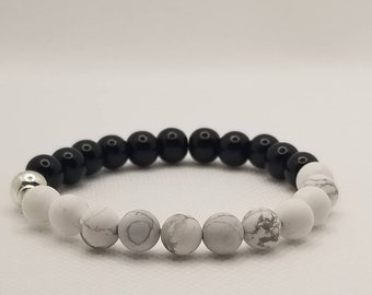 May include: A black and white beaded bracelet with a silver bead. The bracelet is made with black onyx and white howlite beads.