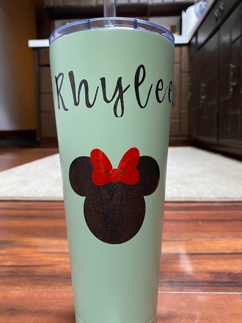 Może przedstawiać: Zielony kubek ze stali nierdzewnej z czarno-czerwonym wzorem Minnie Mouse i imieniem "Rhylee" napisanym czarnym, ozdobnym pismem.