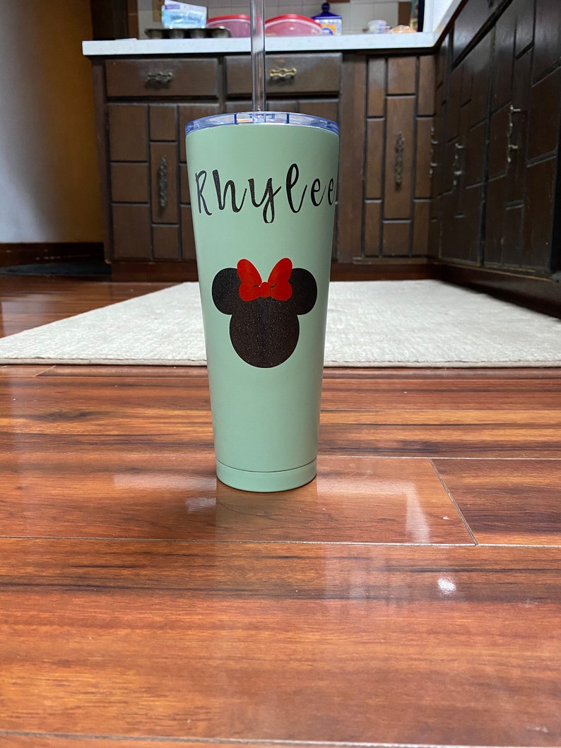 Może przedstawiać: Jasnozielony kubek ze stali nierdzewnej z czarno-czerwonym wzorem Minnie Mouse i imieniem "Rhylee" napisanym czarnymi literami.
