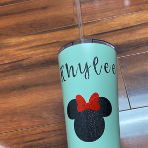 Może przedstawiać: Zielony, wielokrotnego użytku kubek z nadrukiem czarnej głowy Myszki Miki z brokatem i imieniem "Rhylee" napisanym czarnym, ozdobnym pismem. Kubek ma przezroczystą słomkę z tworzywa sztucznego.