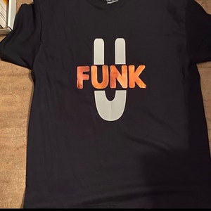 May include: Black t-shirt with a white and orange graphic of the word "FUNK" with a stylised "U" in the centre.