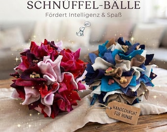 May include: Two spherical dog enrichment toys made of layered fabric strips. One ball features shades of red, pink, and burgundy, while the other displays blue, white, and brown. Text reads: SCHNÜFFEL-BÄLLE, Fördert Intelligenz & Spaß, and HANDGEMACHT FÜR HUNDE.