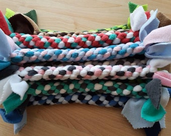 Pode incluir: Uma pilha de brinquedos mastigáveis ​​trançados para cães de várias cores com pontas de lã felpuda. Os brinquedos são feitos com diferentes cores de tecido de lã felpuda, incluindo vermelho, azul, verde, branco e preto.
