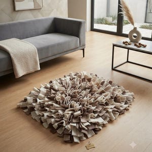 Könnte beinhalten: Eine quadratische Schnüffelmatte mit geschichteten Filzstreifen in Creme-, Beige- und Brauntönen. Die Matte hat eine dichte, zottelige Textur, die durch zahlreiche Stoffschlaufen entsteht. Ein kleines, knochenförmiges Holzschild liegt am unteren Rand.