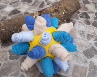 May include: A yellow ball covered in blue and beige fabric rolls. The fabric is rolled into a spiral shape and is sewn together to create a ball.