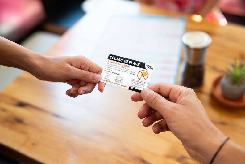 May include: A white card with black text that reads "Celiac Disease I cannot eat gluten" and a red circle with a diagonal line through a wheat stalk. The card also includes a list of ingredients that contain gluten. The card is being passed from one person to another.