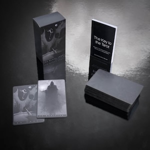 May include: A black box with the text "The Black Tarot" on the front. A black book with the text "The Key to the Tarot" on the front. A stack of black tarot cards.