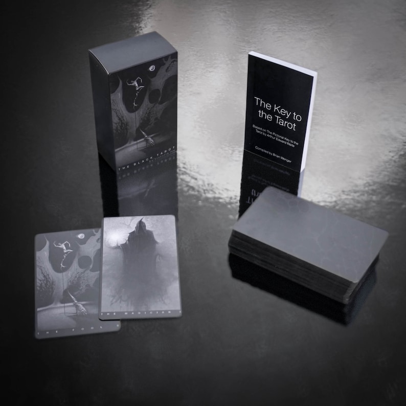 May include: A black box with the text "The Black Tarot" on the front. A black book with the text "The Key to the Tarot" on the front. A stack of black tarot cards.