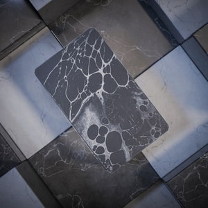 May include: A dark gray phone case with a white marbled design. The case has a textured surface and a unique pattern.