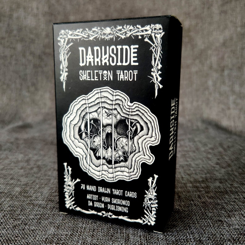 May include: A black box with a silver skull design and the text "DARKSIDE SKELETON TAROT" on the front. The box contains 78 hand-drawn tarot cards. The artist is Wury Shorowod and the publisher is Da Brich Publishing.